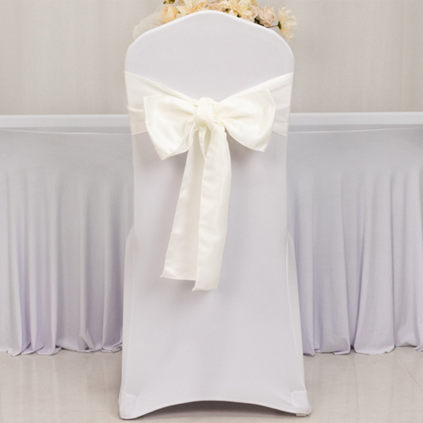 Ivory satin chair sash with bow on a white chair.