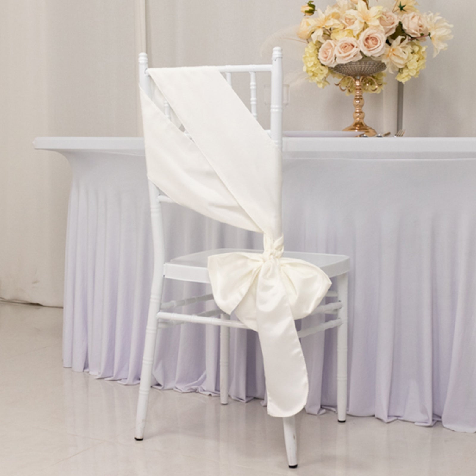 Ivory satin chair sash with bow on a white chair.