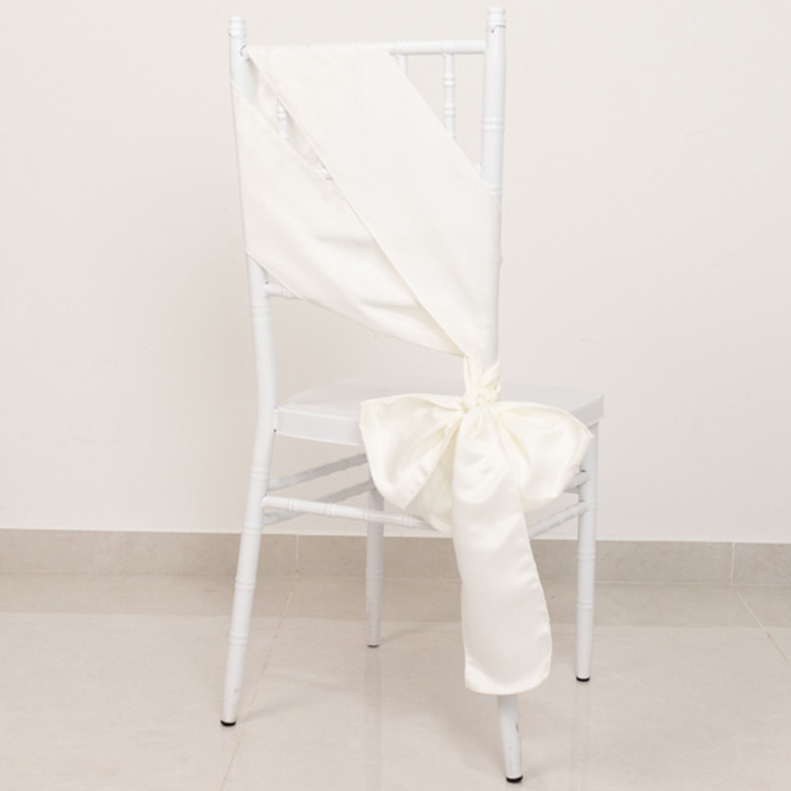 Ivory satin chair sash tied in a bow on a white chair.