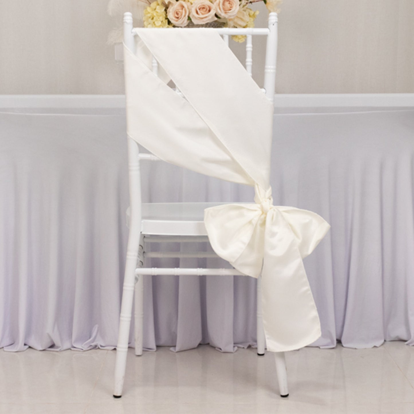 Ivory satin chair sash bow tied on a white chair.