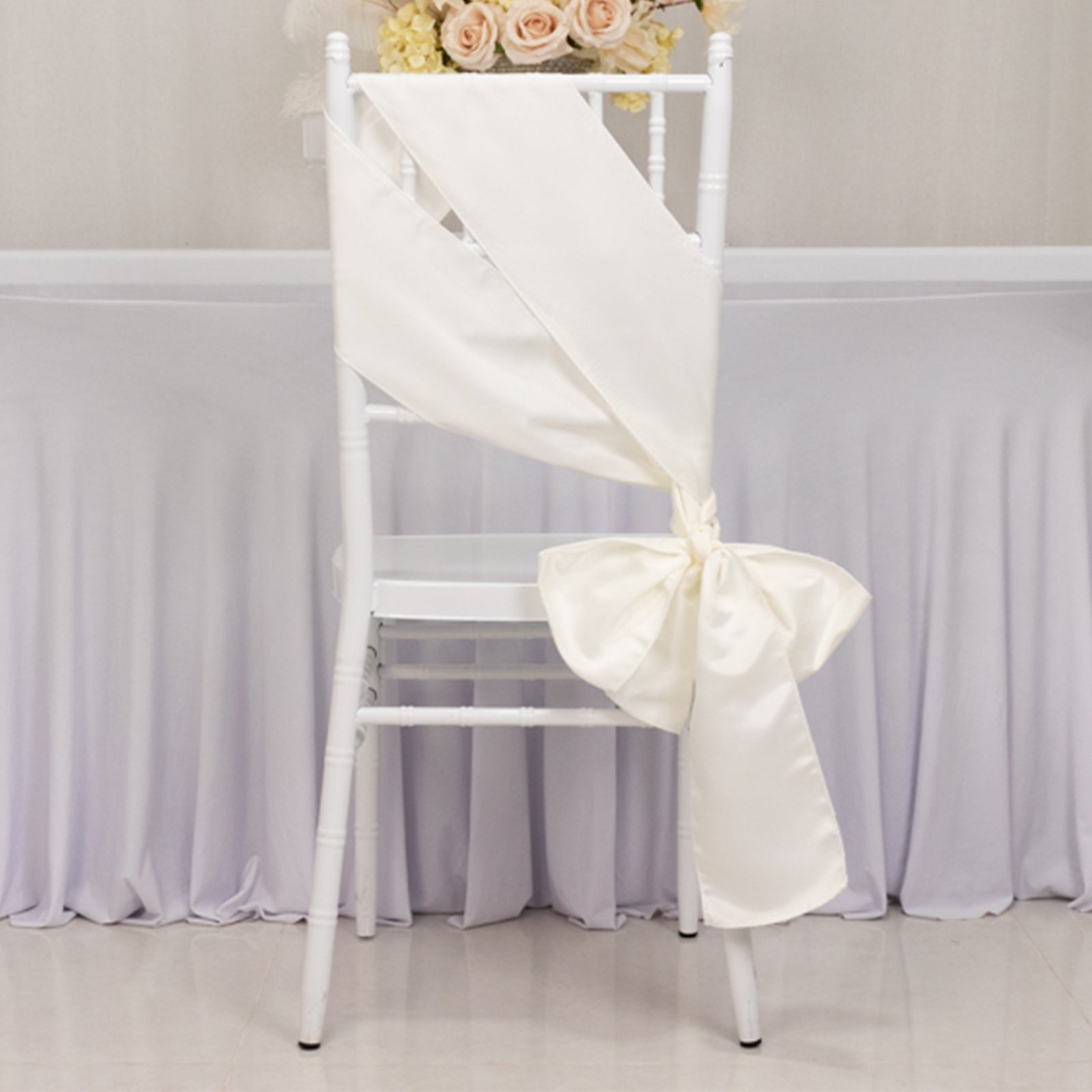 Ivory satin chair sash bow tied on a white chair.