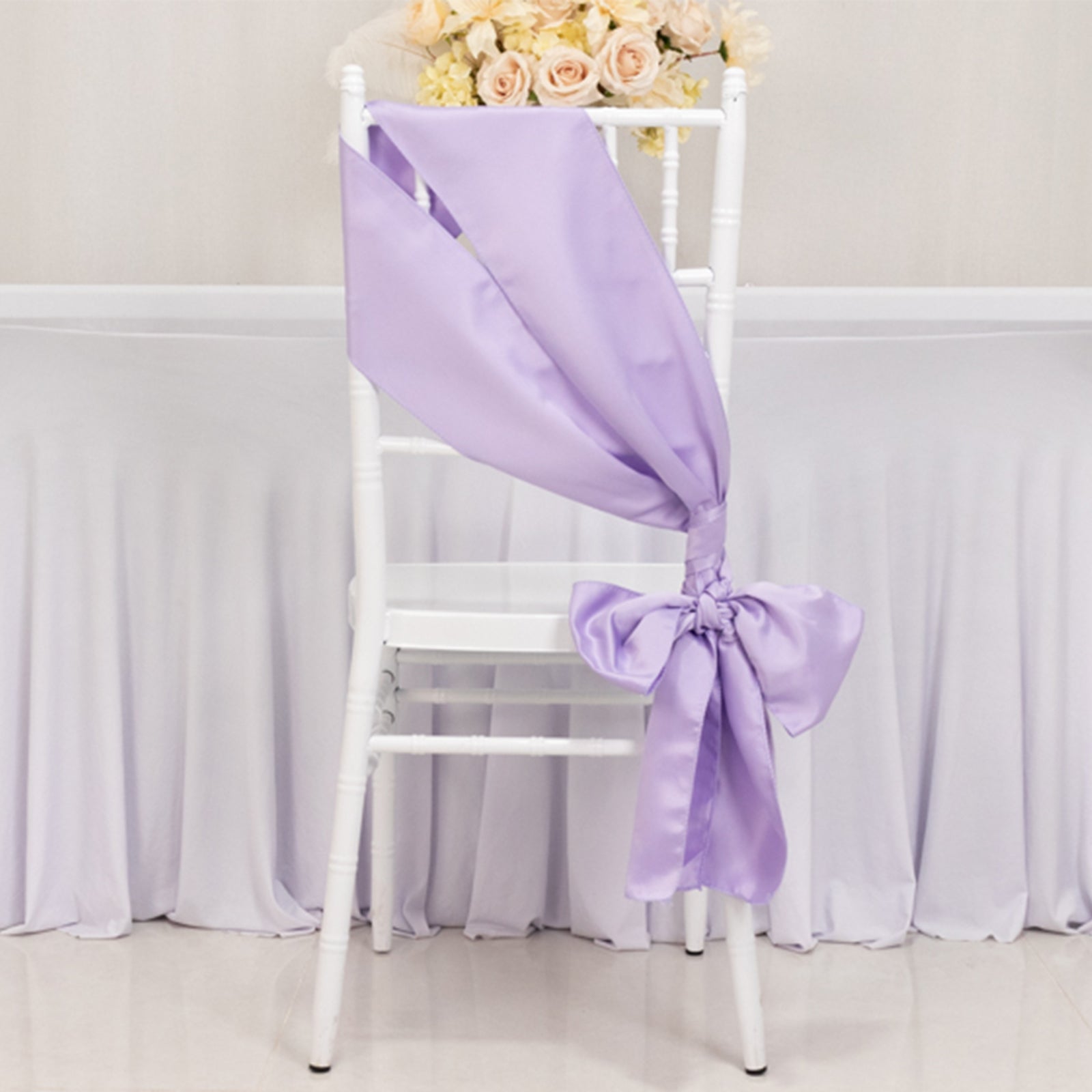 Lavender satin chair sash tied in a bow on a white chair.