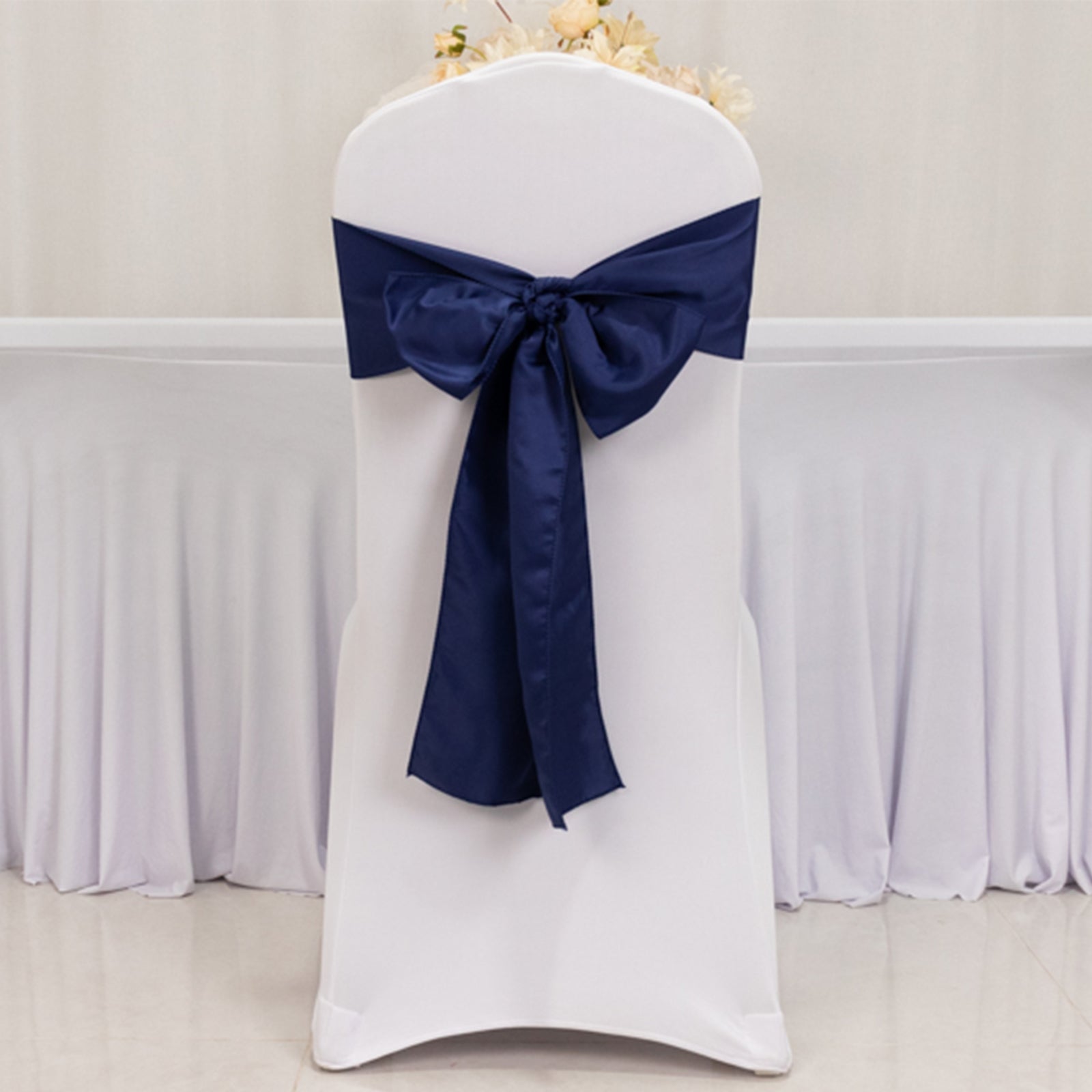 Navy blue satin chair sash bow on a white chair.