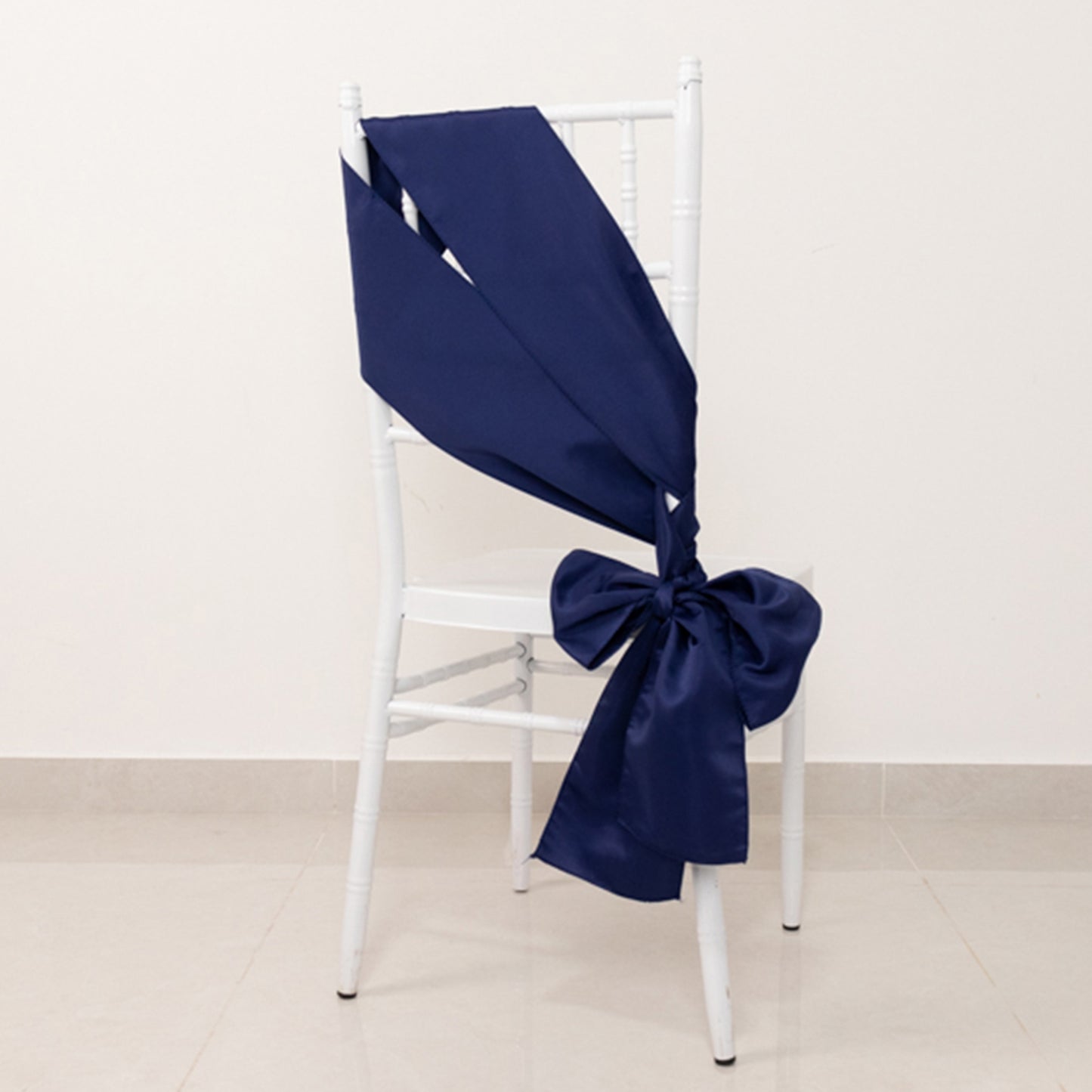 Navy blue satin chair sash elegantly tied on a white chair.