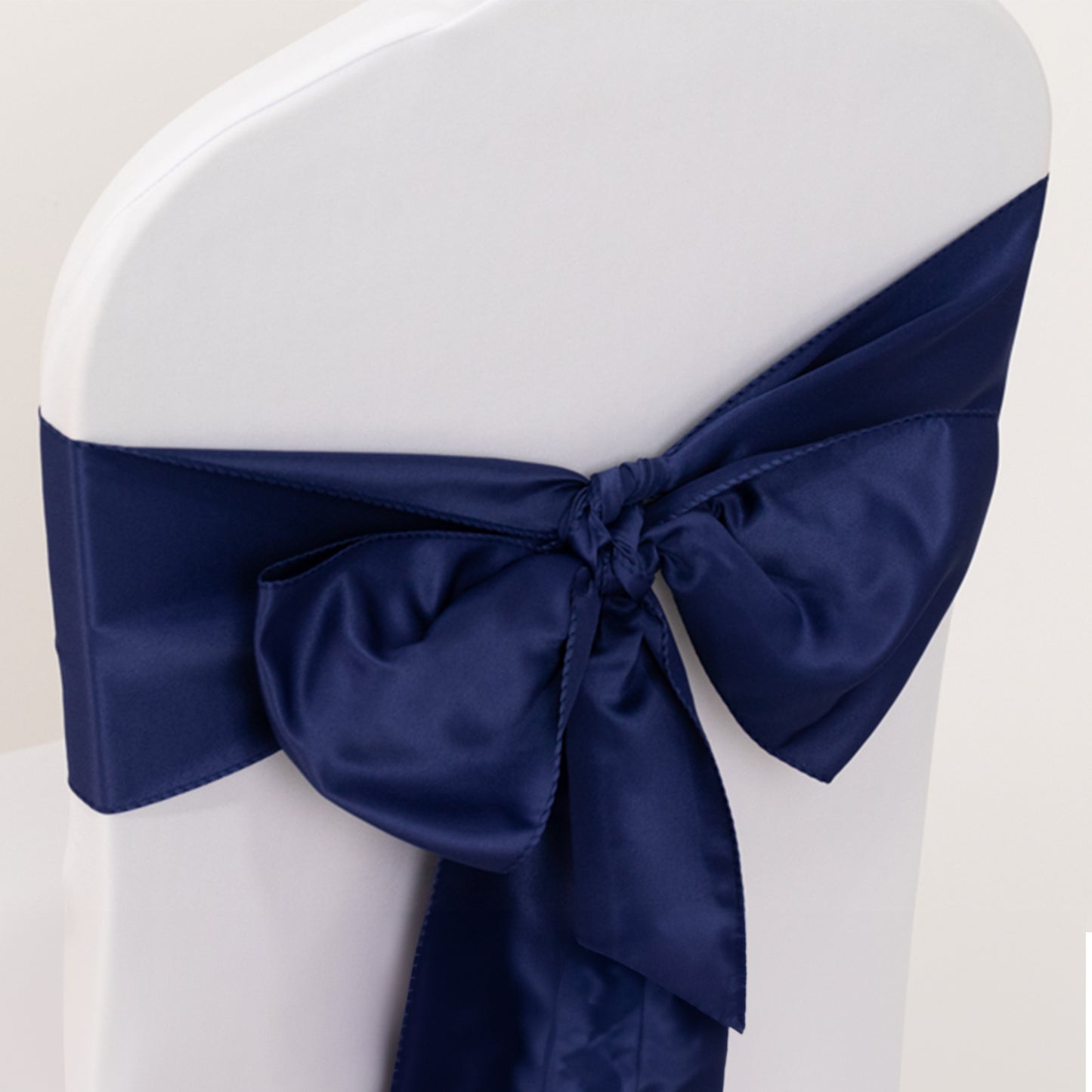 Navy blue satin chair sash tied in a bow on a white chair.