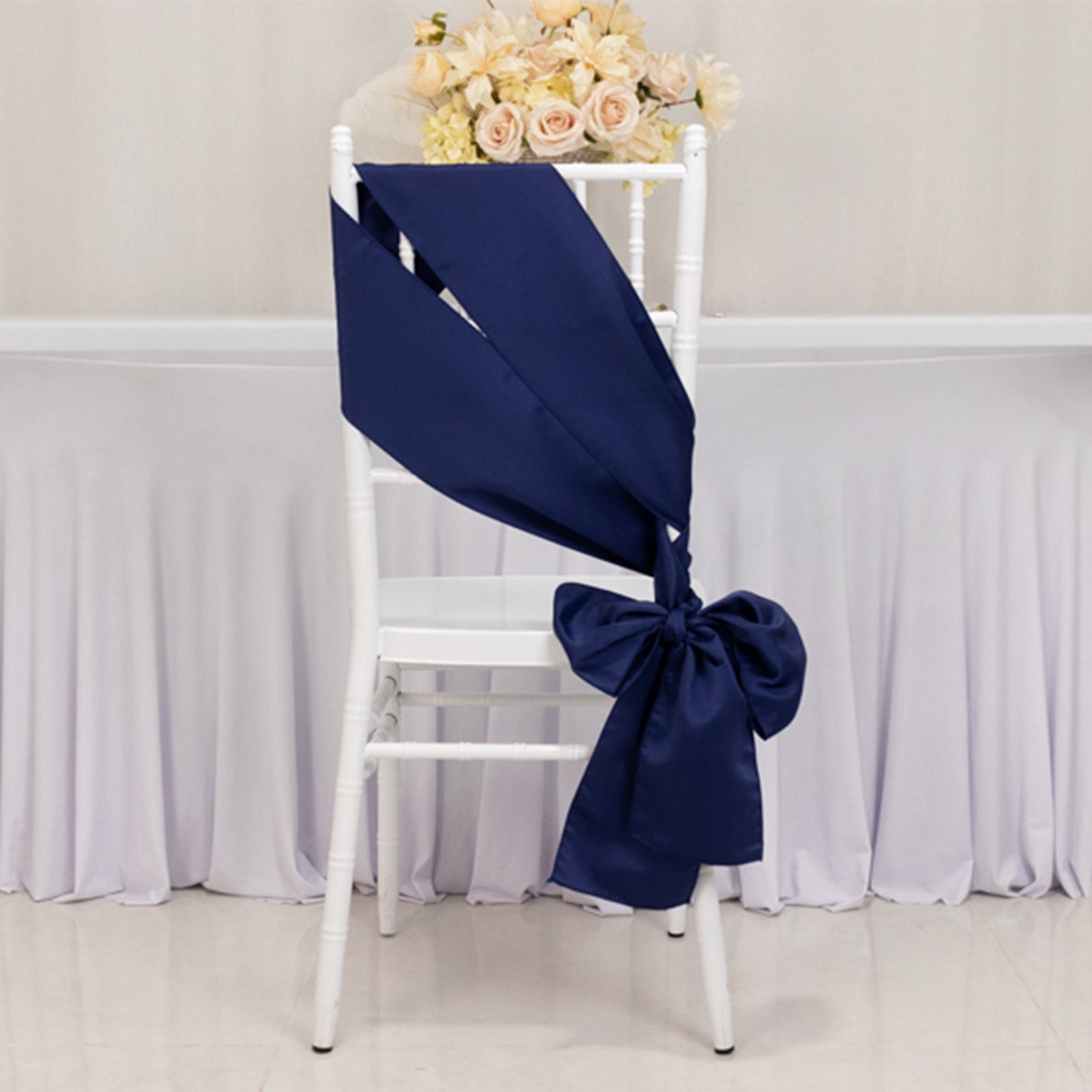 Navy blue satin chair sash tied in a bow on a white chair.