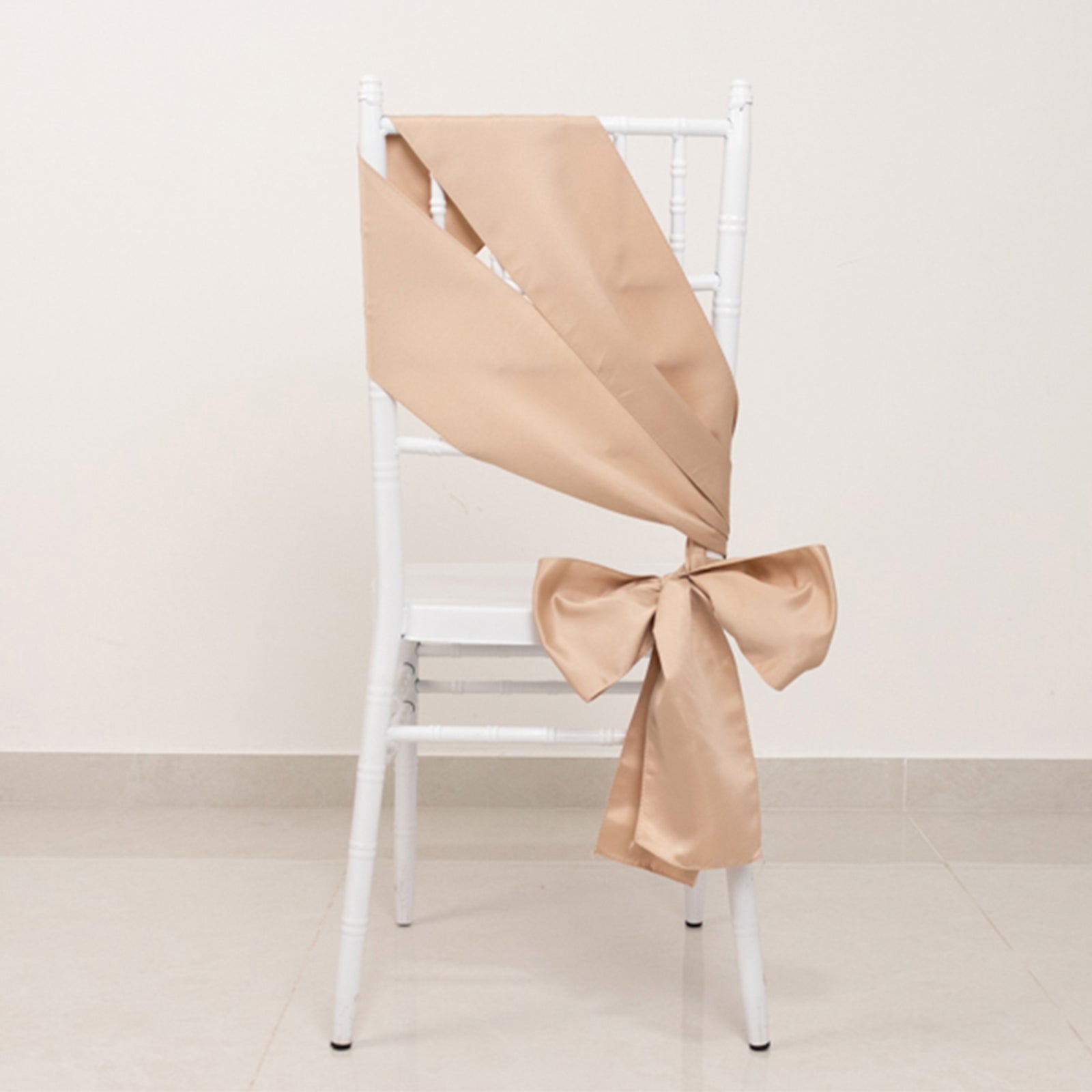 Nude satin chair sash bow elegantly tied on a white chair.