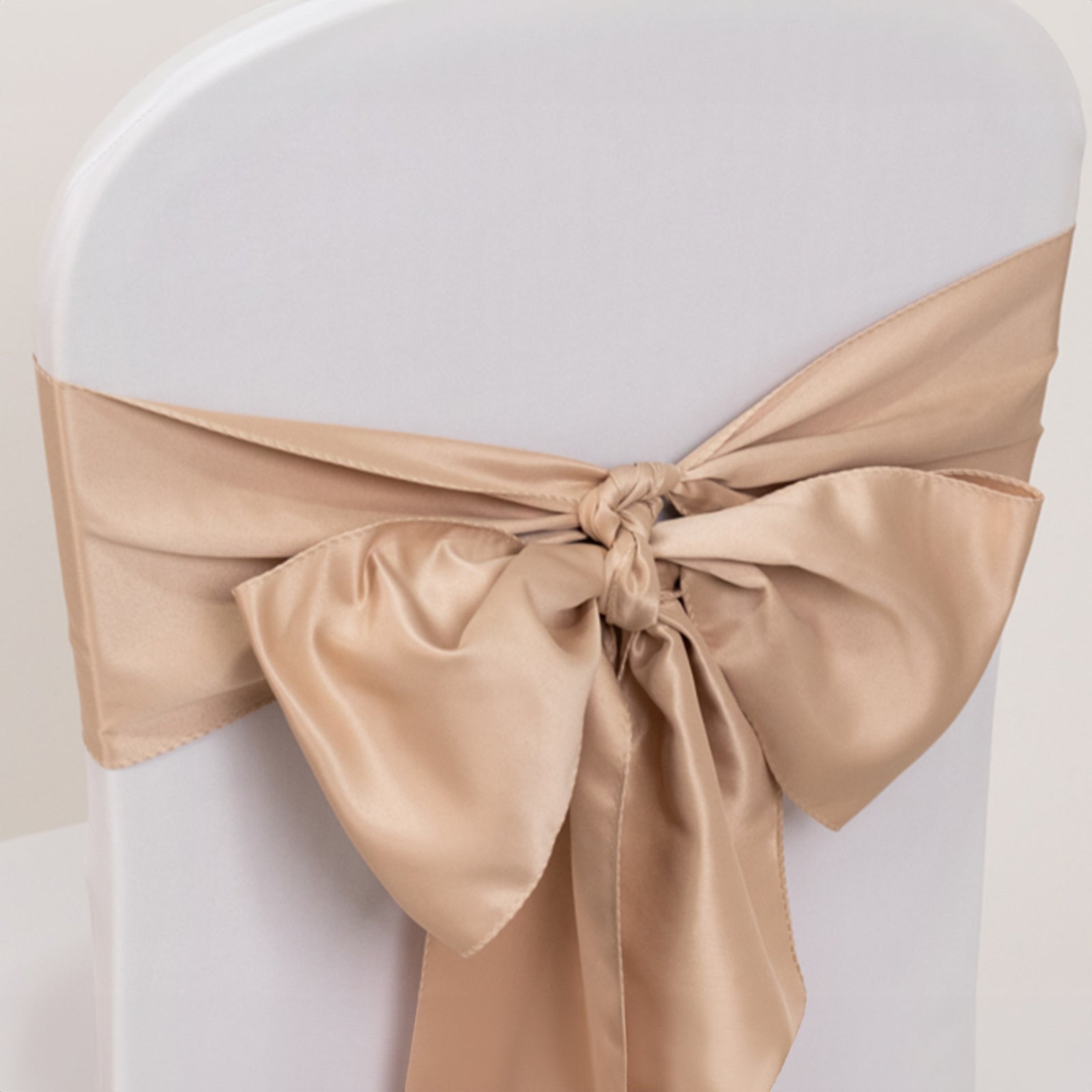 Nude satin chair sash bow on a white chair.