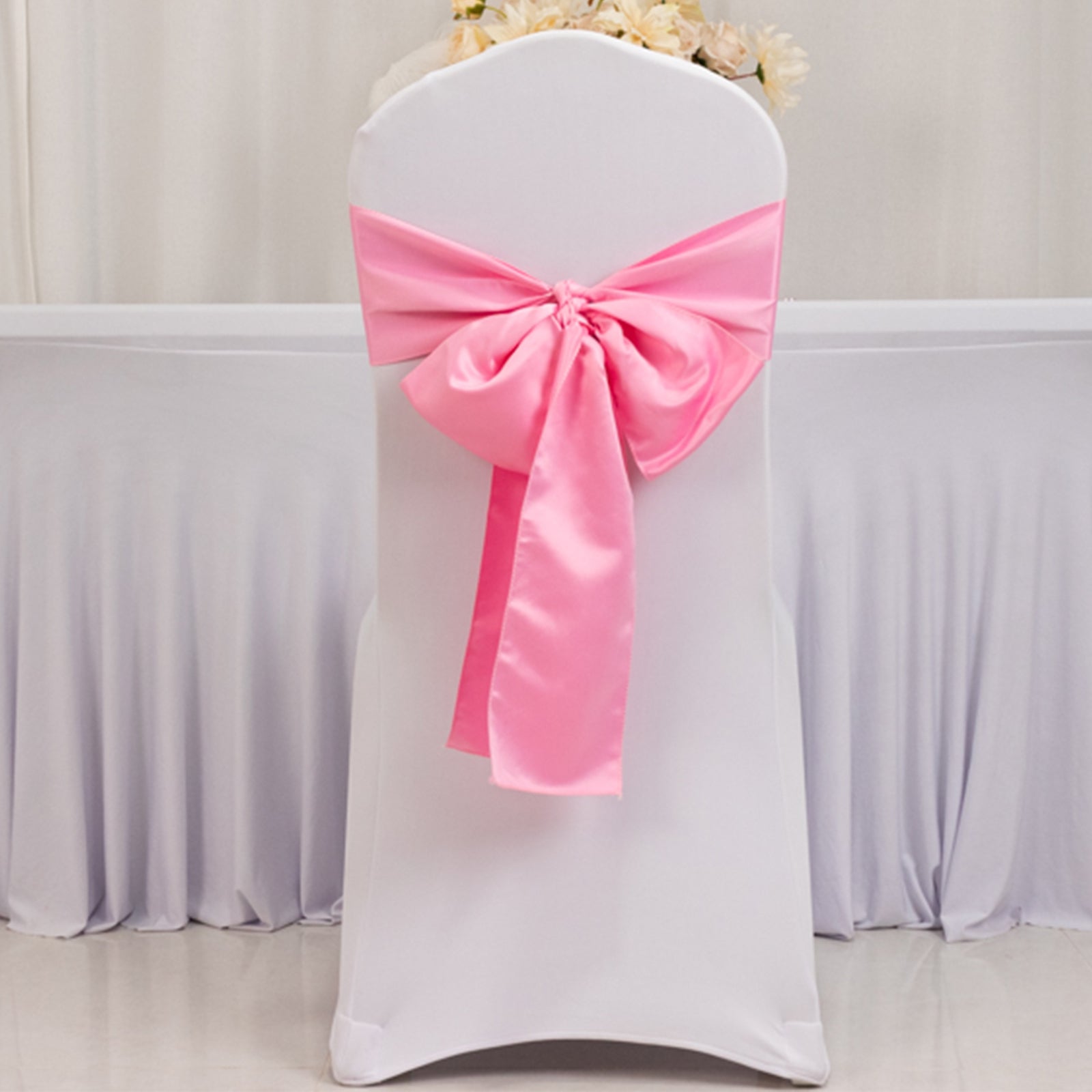 Pink satin chair sash bow on a white chair.
