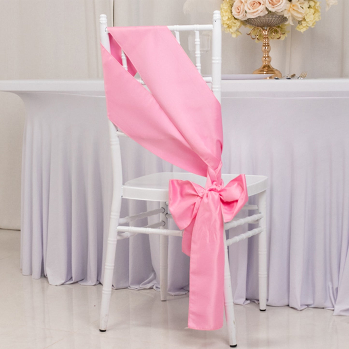 Pink satin chair sash bow on a white chair.