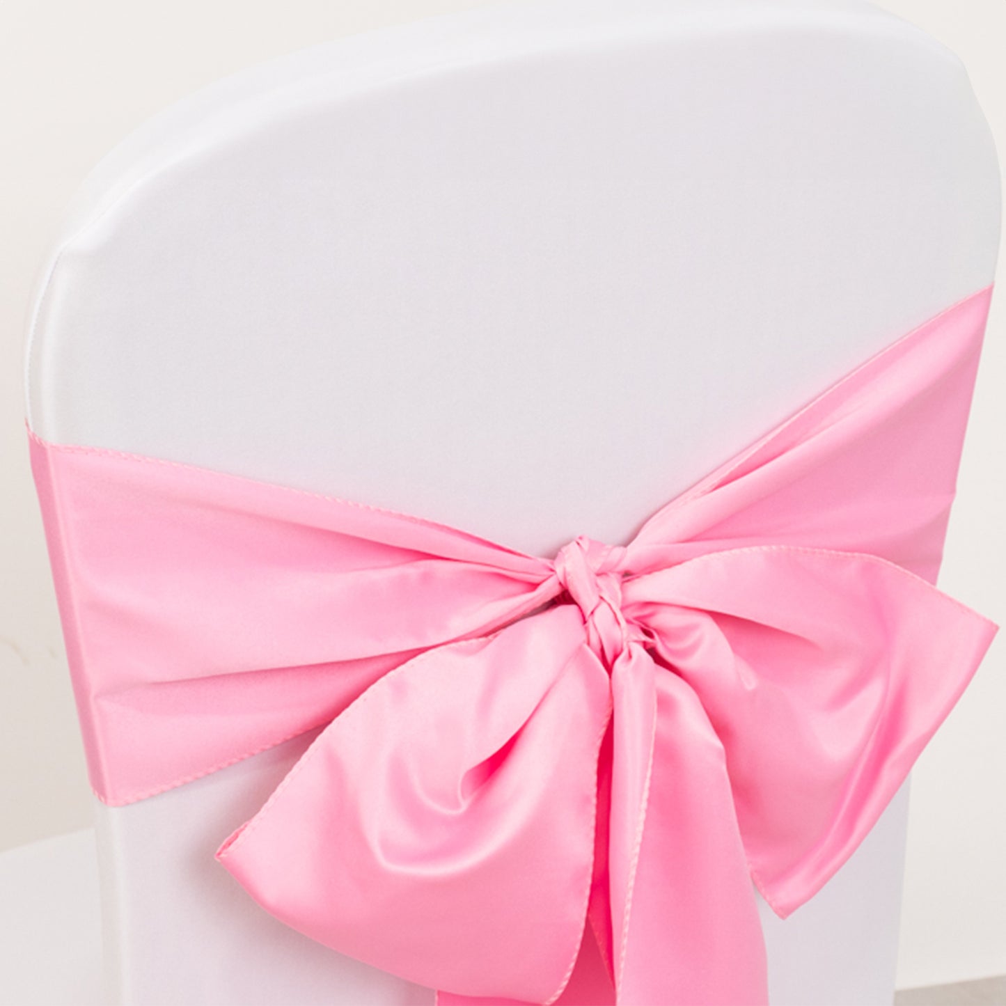 Pink satin chair sash bow on a white chair.