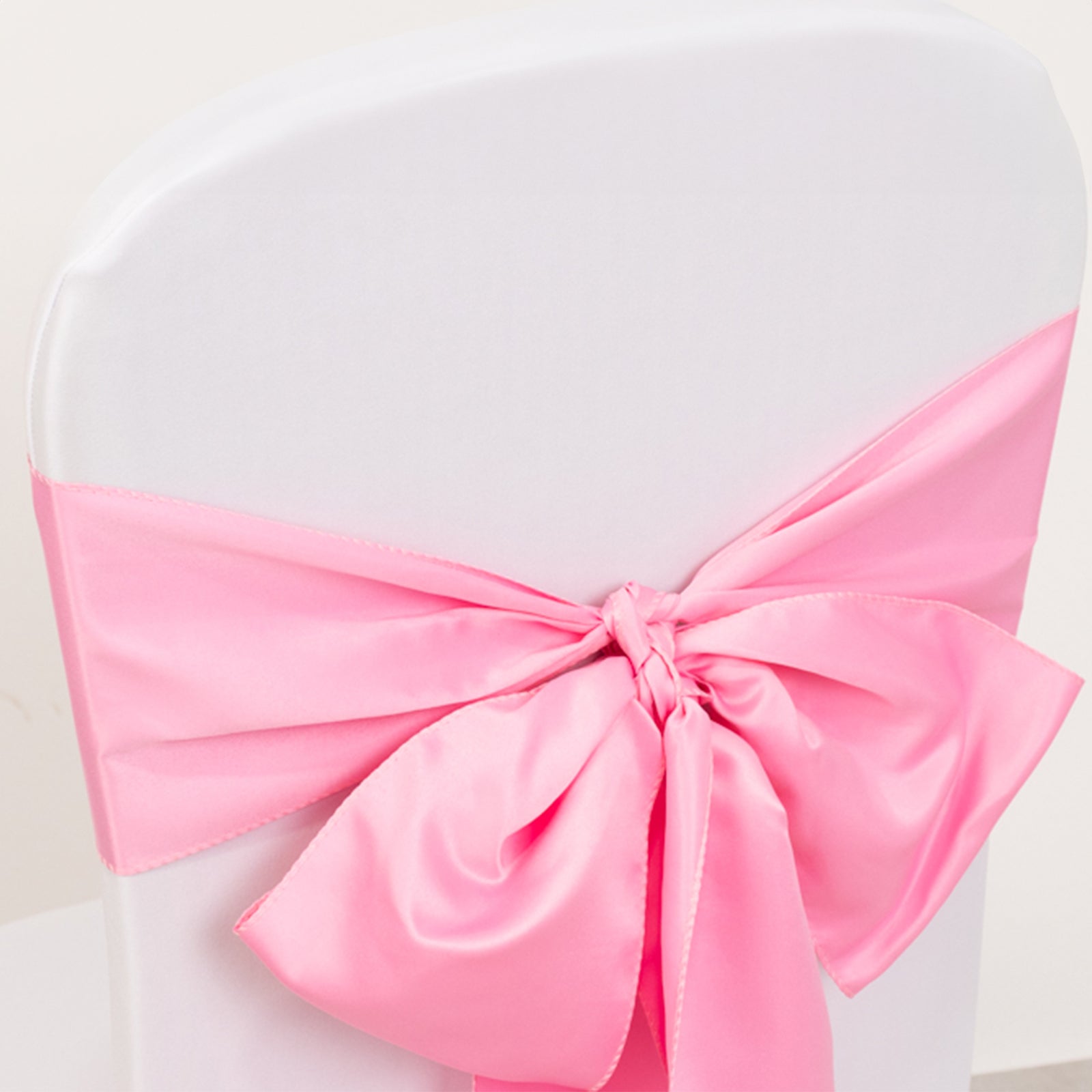 Pink satin chair sash bow on a white chair.