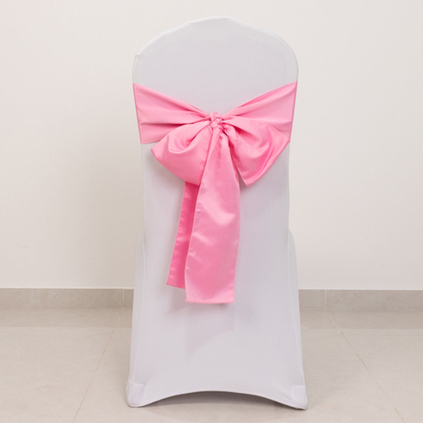 Pink satin chair sash bow on a white chair.