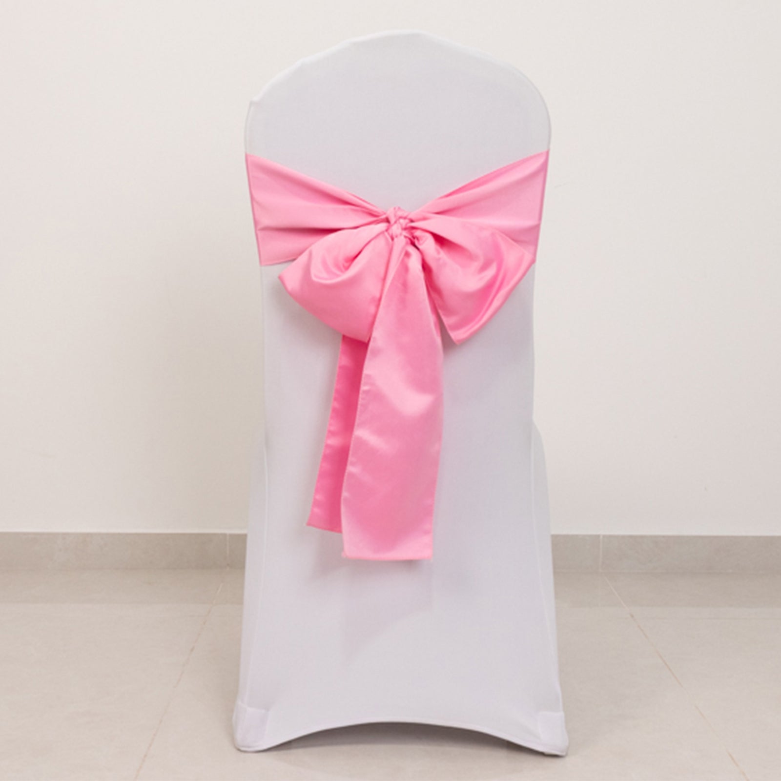 Pink satin chair sash bow on a white chair.