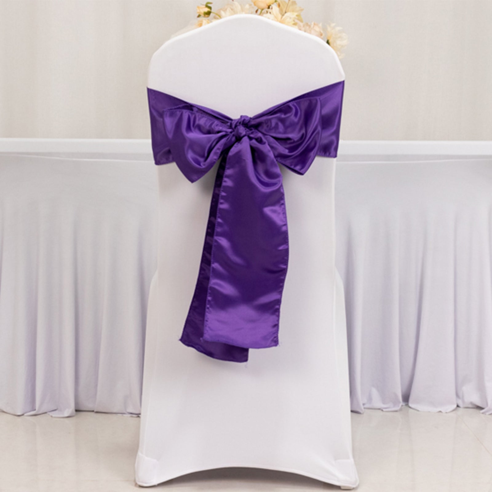 Purple satin chair sash bow on a white chair, perfect for events.