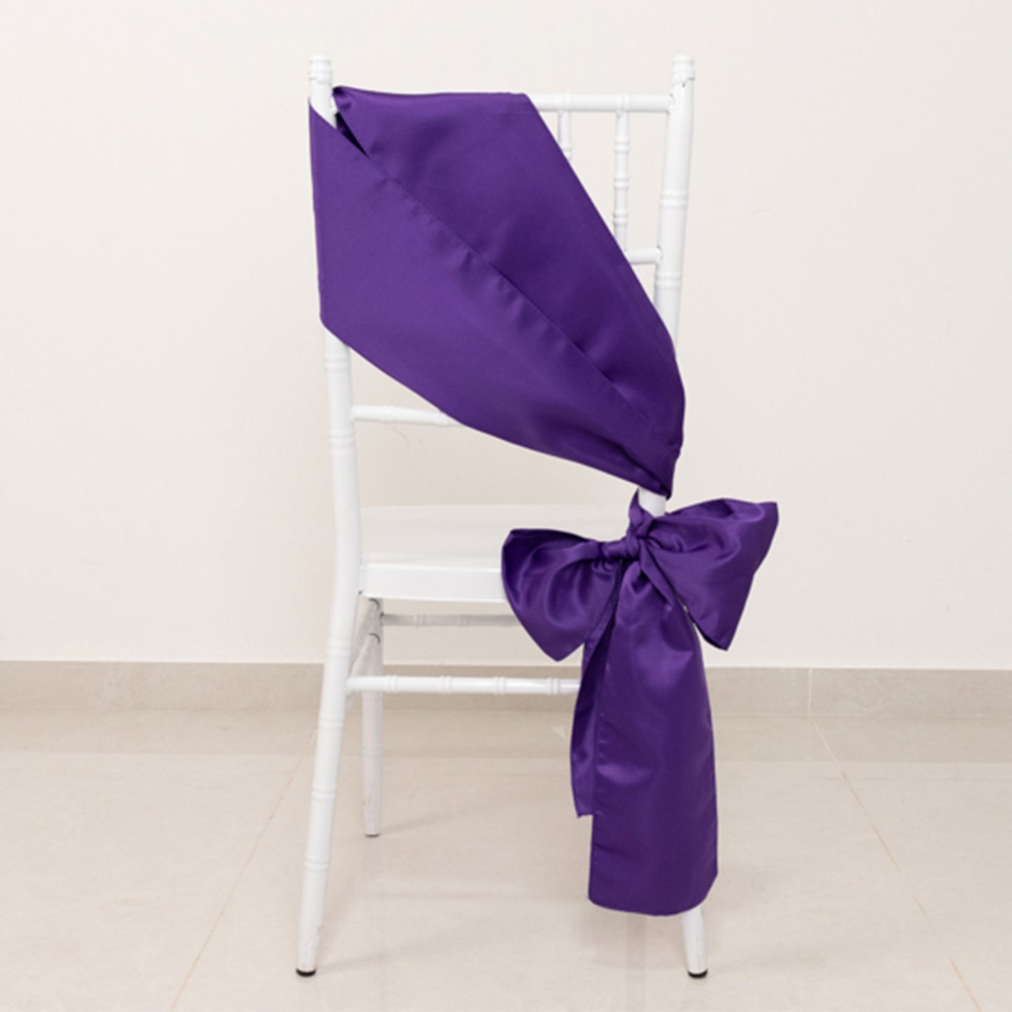 Purple satin chair sash bow on a white chair.