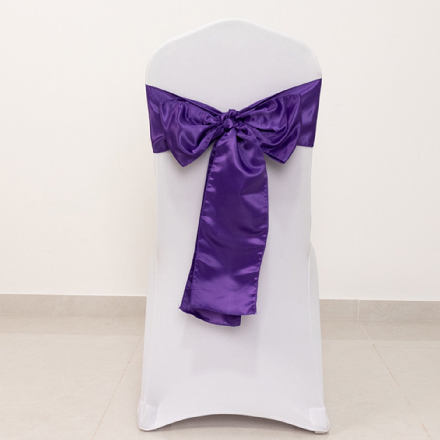 Purple satin chair sash bow on a white chair.