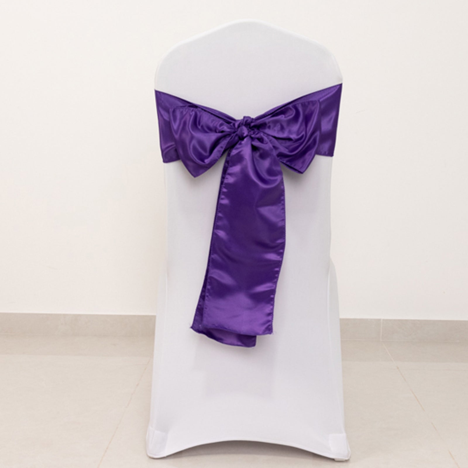 Purple satin chair sash bow on a white chair.