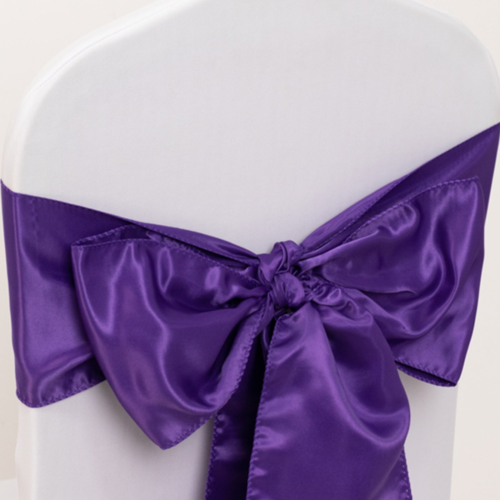 Purple satin chair sash bow on a white chair.