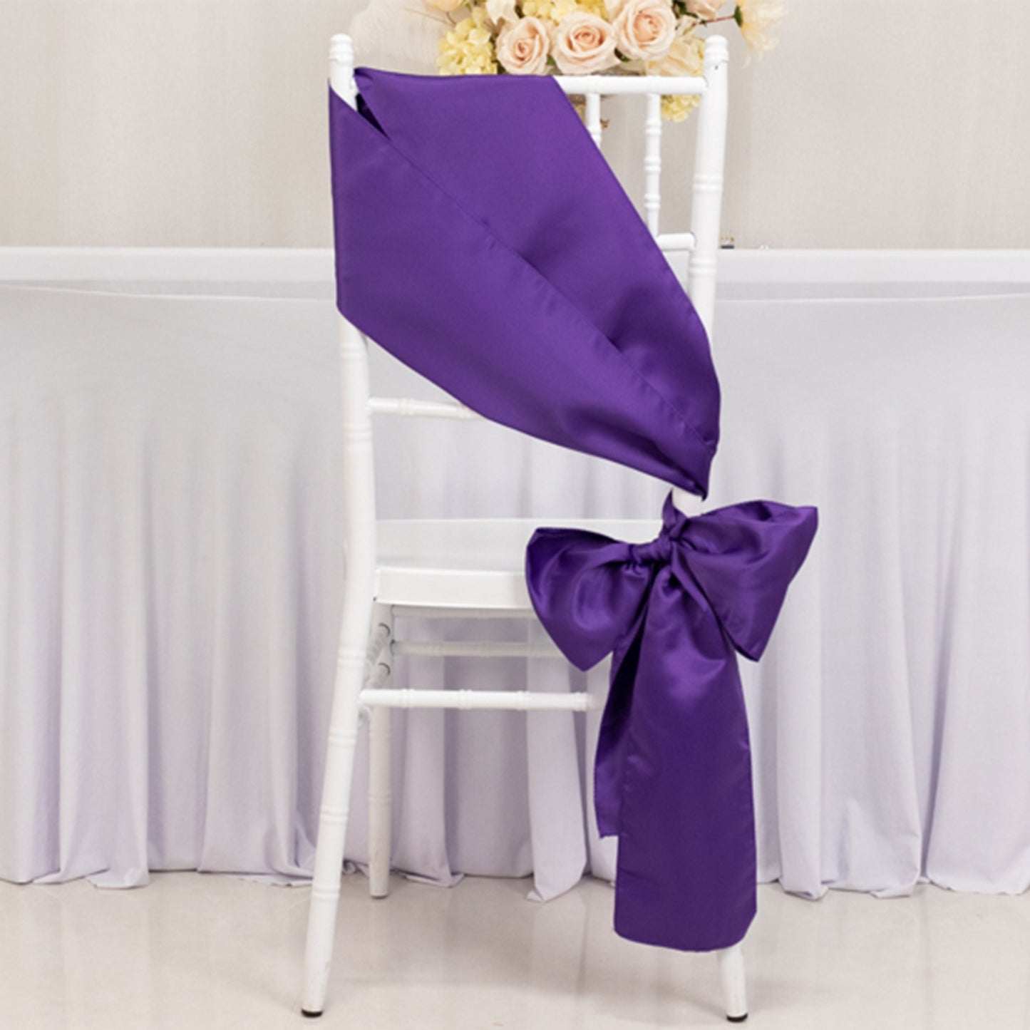 Purple satin chair sash and bow on a white chair.