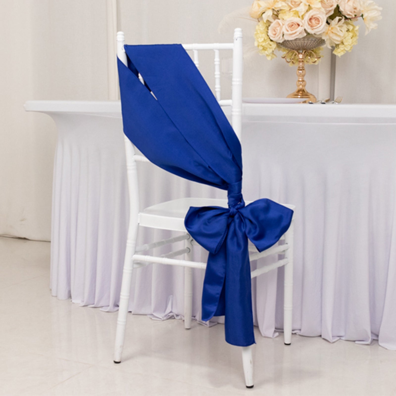Royal blue satin chair sash tied in a bow on a white chair.