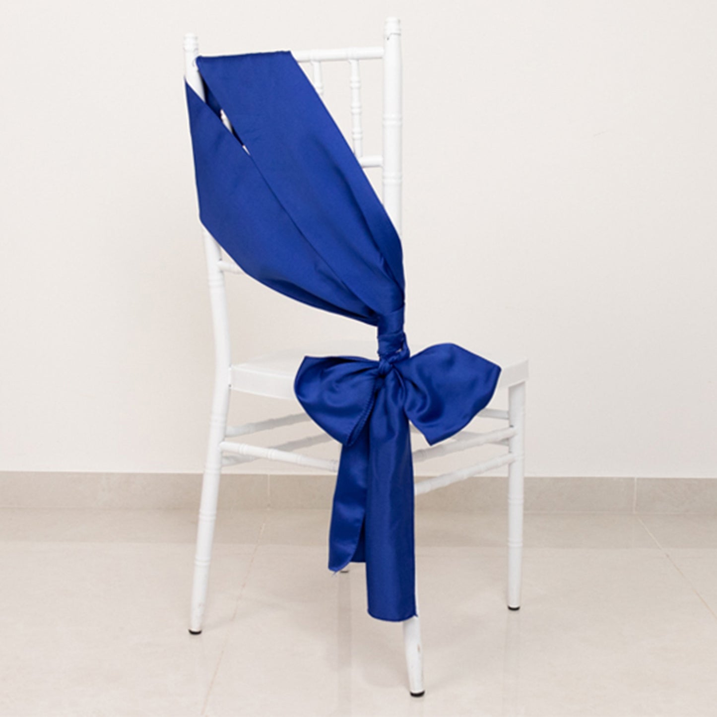 Royal blue satin chair sash tied in a bow on a white chair.