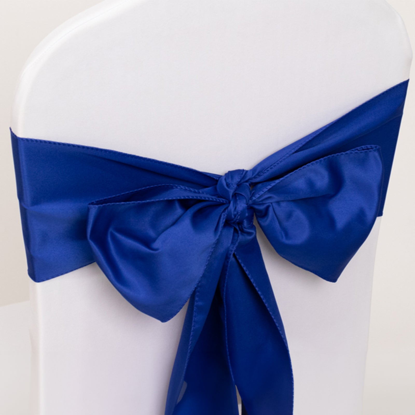 Royal blue satin chair sash tied in a bow on a white chair.