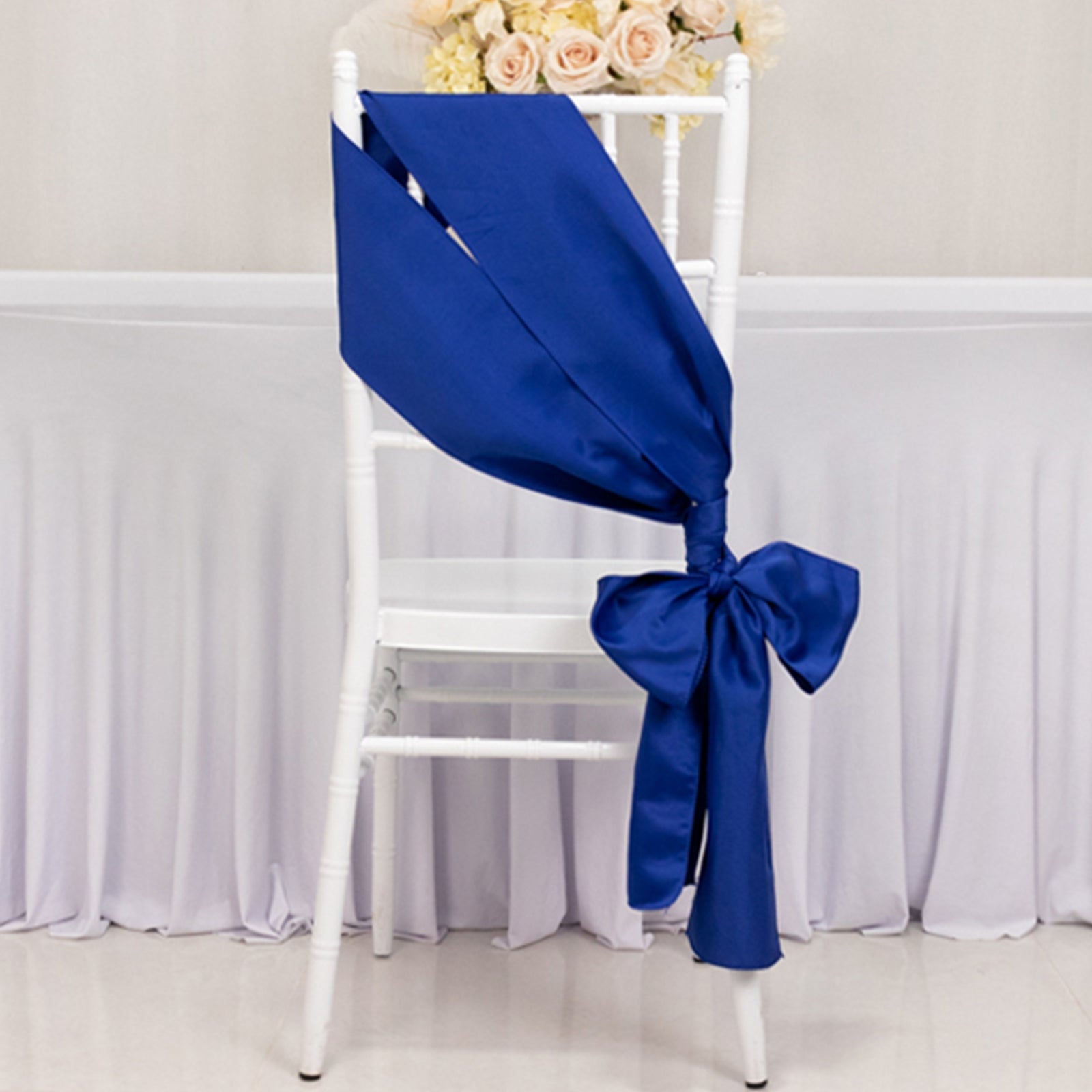 Royal blue satin chair sash tied in a bow on a white chair.