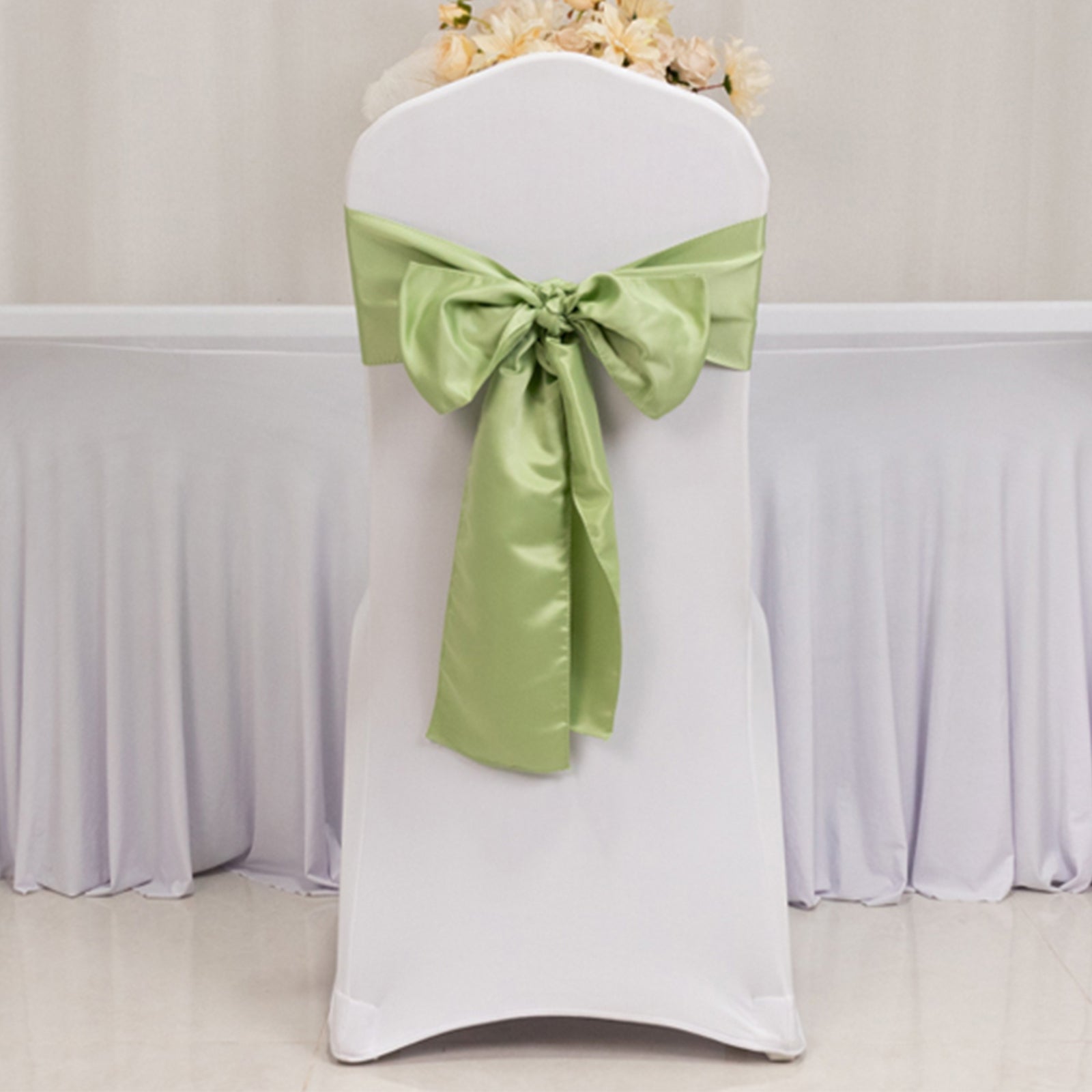 Sage green satin chair sash tied in a bow on a white chair.