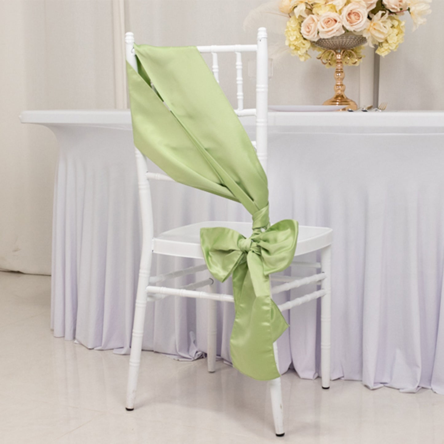 Sage green satin chair sash with a bow on a white chair.