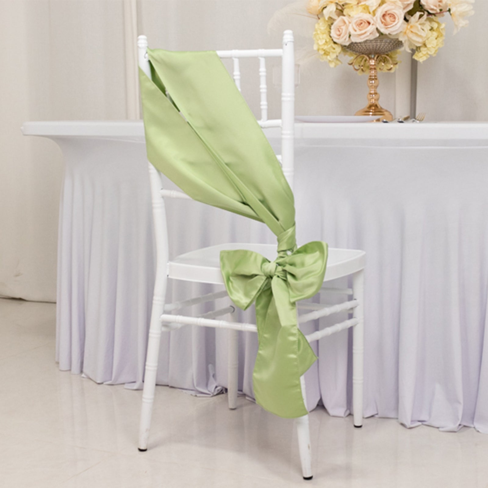 Sage green satin chair sash with a bow on a white chair.