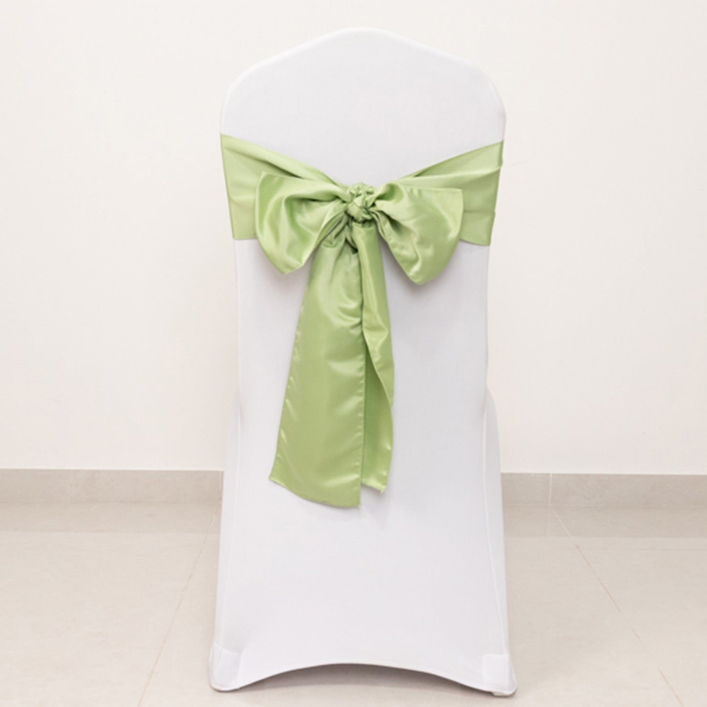 Sage green satin chair sash tied in a bow on a white chair.