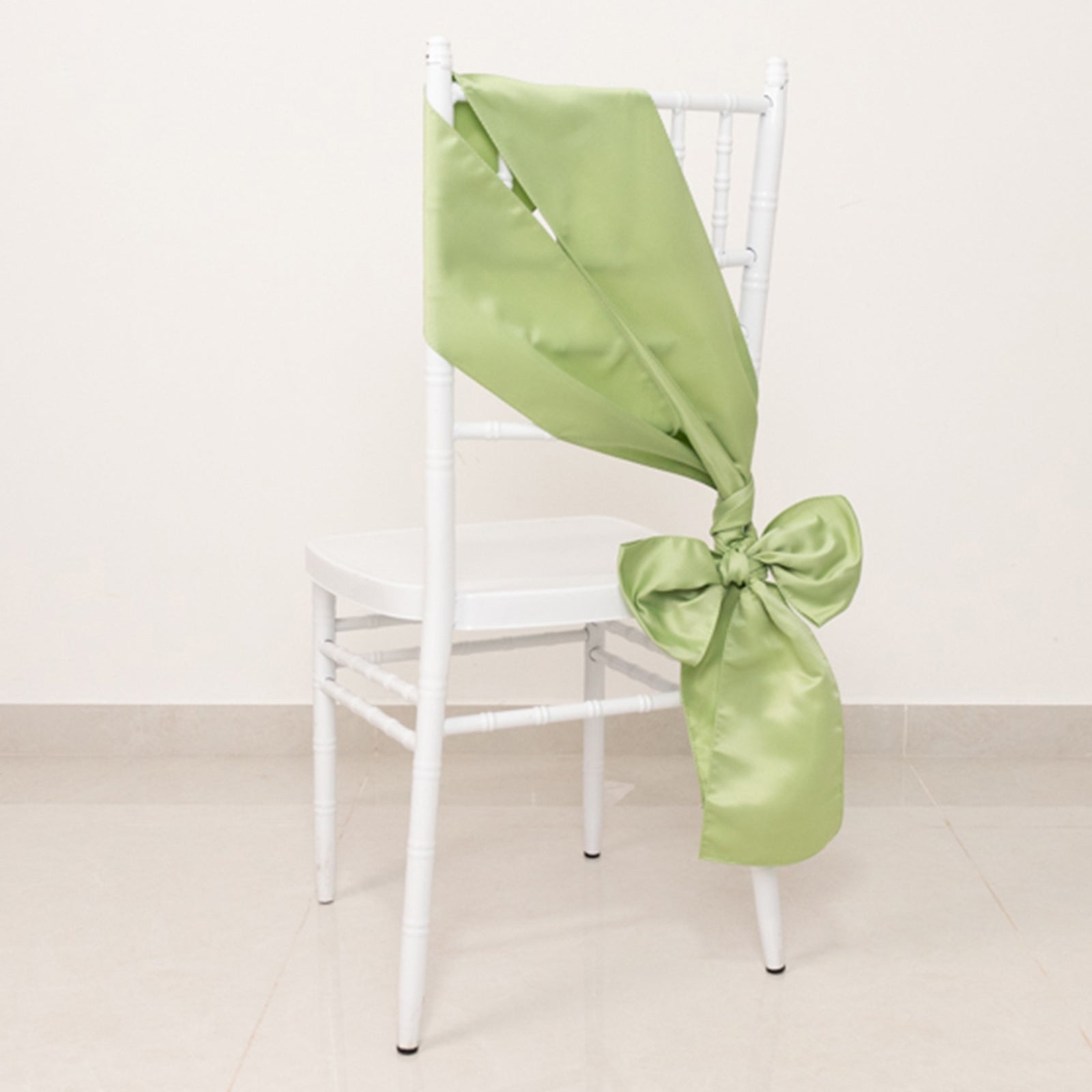 Sage green satin chair sash with bow on a white chair.