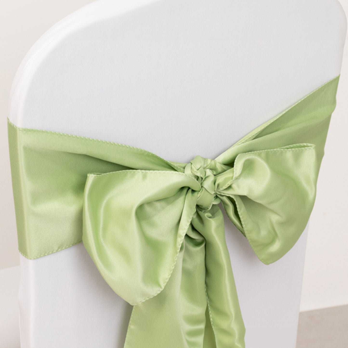 Sage green satin chair sash bow on a white chair.