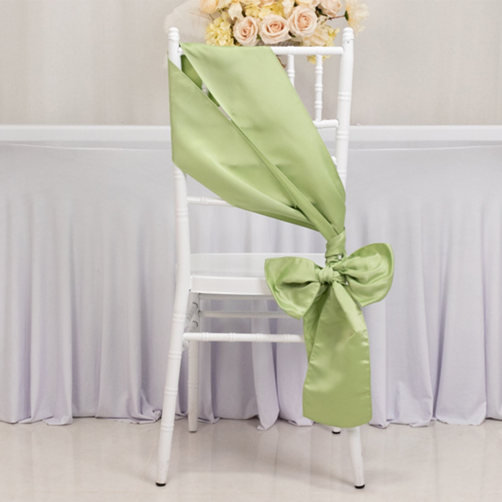 Sage green satin chair sash tied in a bow on a white chair.