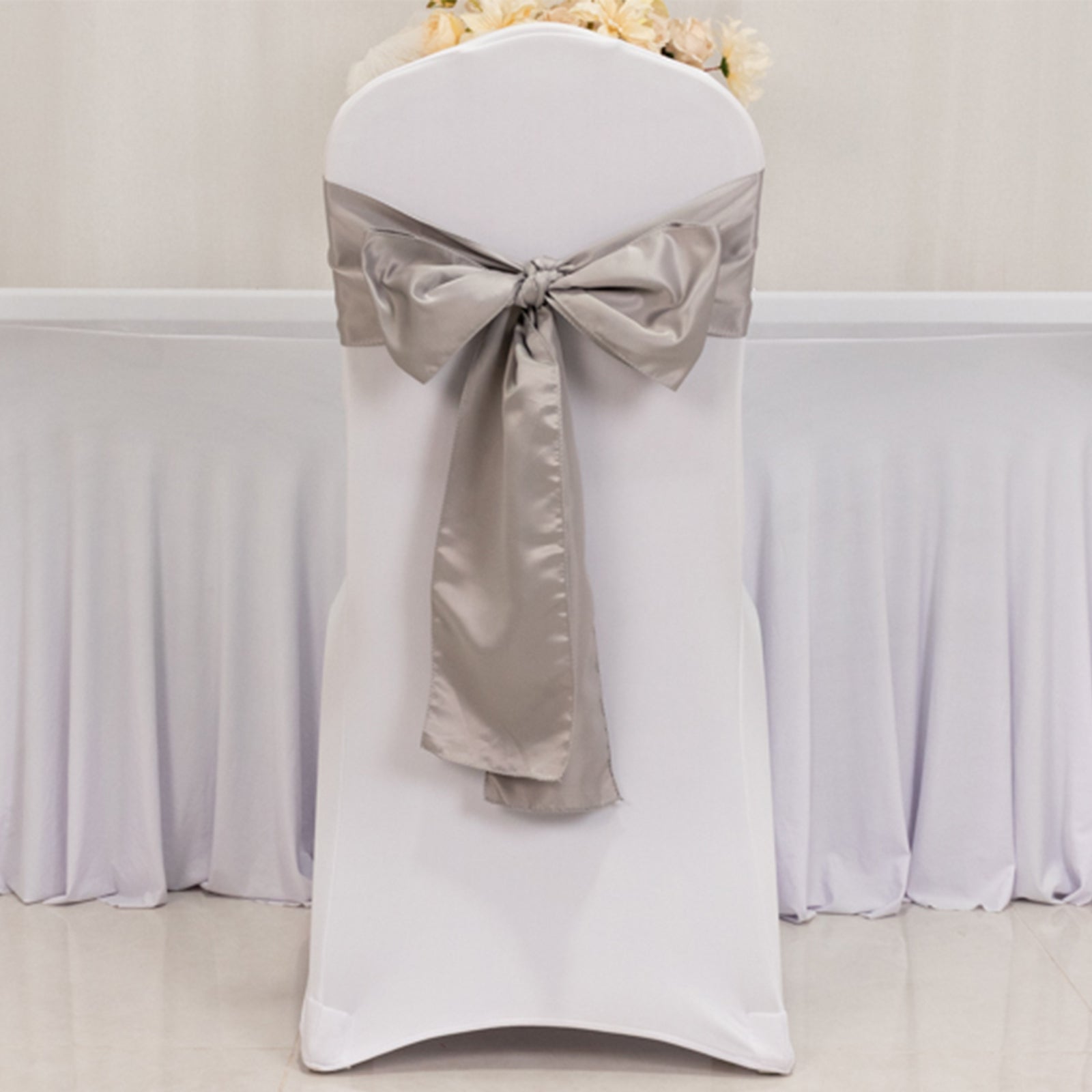 Silver satin chair sash bow on a white chair.