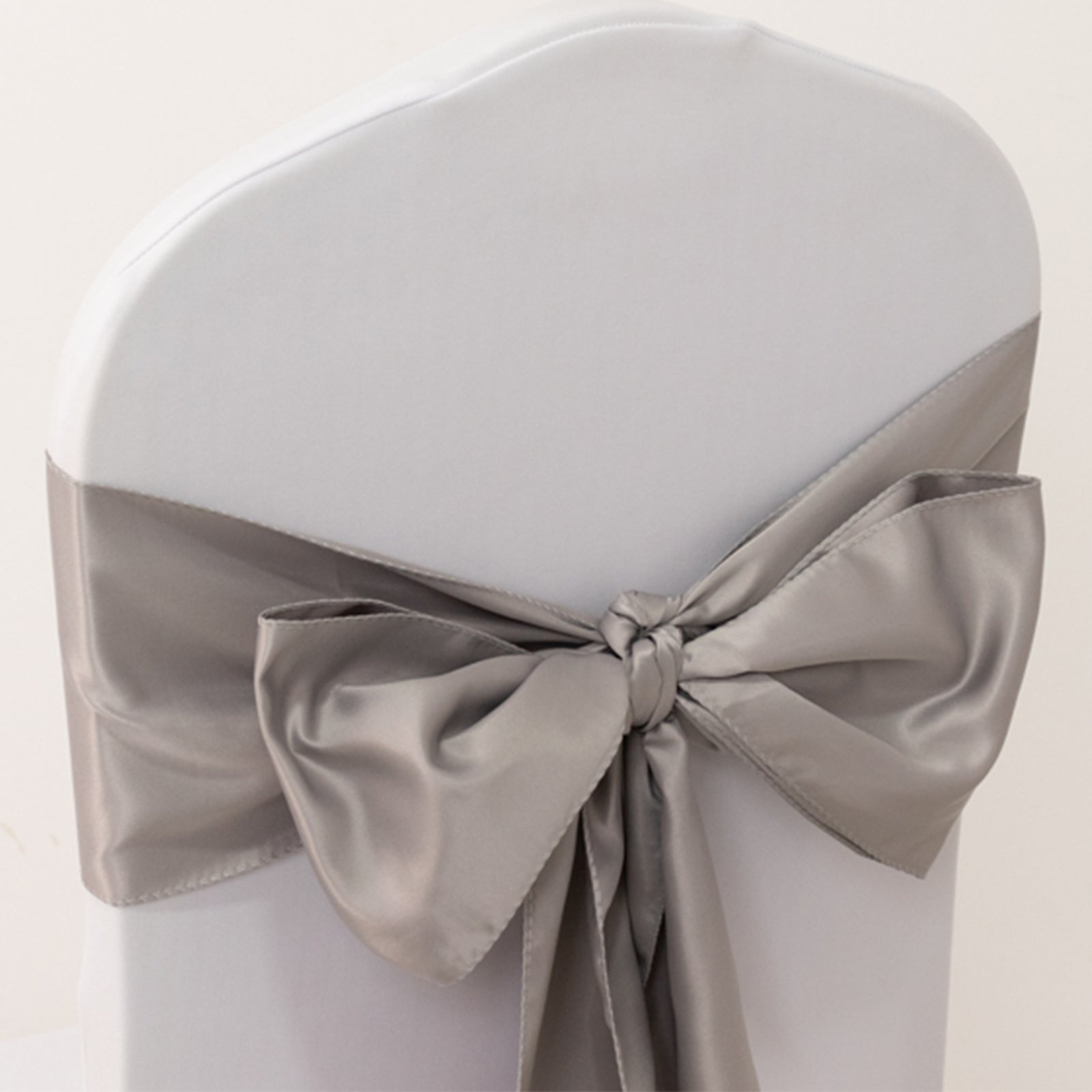 Silver satin chair sash tied in a bow on a white chair.