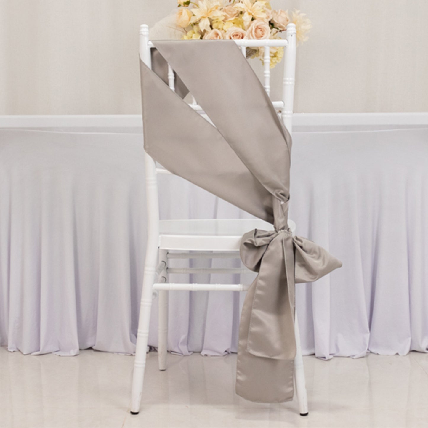 Silver satin chair sash elegantly tied on a white chair.