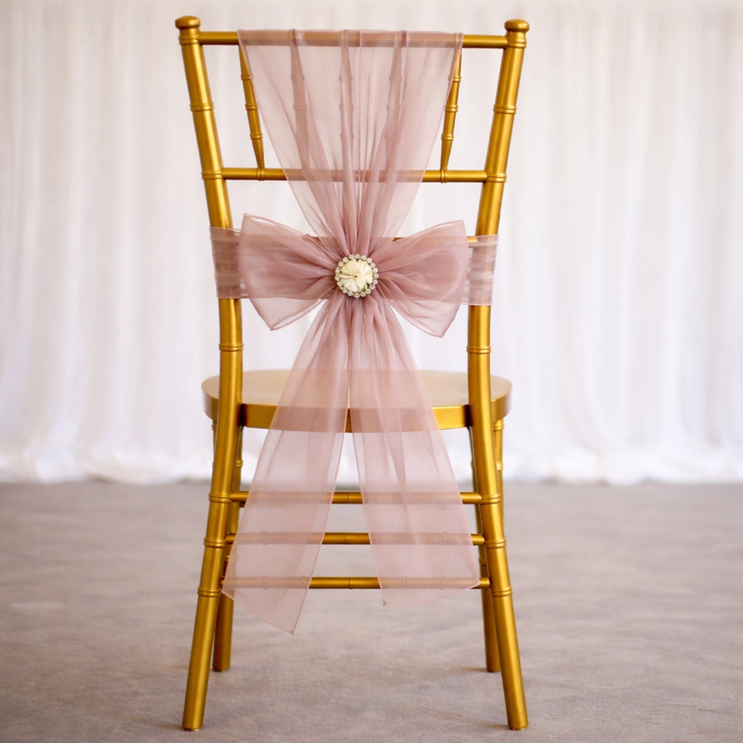 Dusty rose organza chair sash with bow on a gold chair.