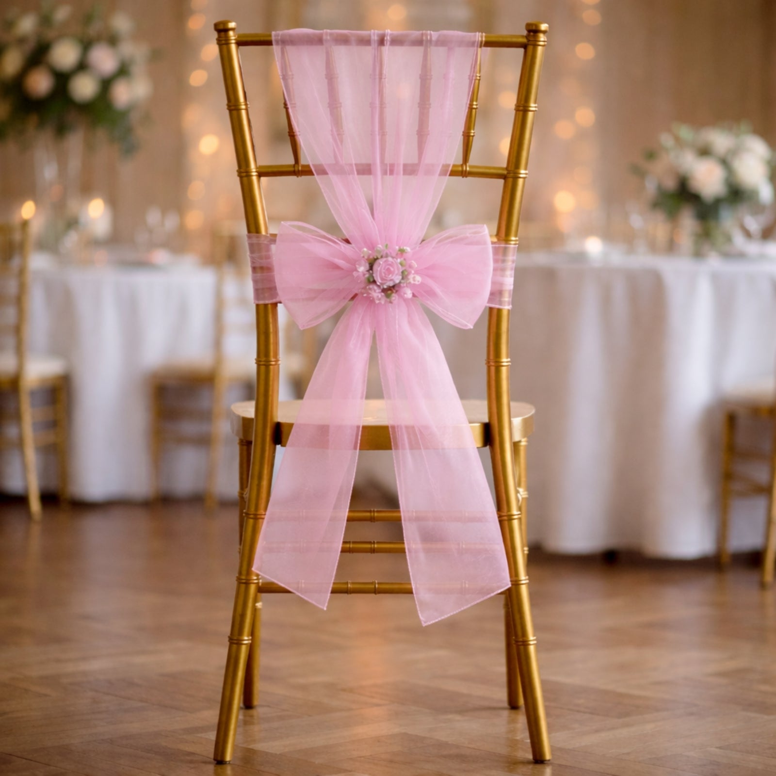 Pink organza chair sash tied in a bow on a gold chair at a wedding setting.