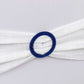 Royal blue diamond circle napkin ring brooch on white fabric.