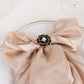 Black pearl floral metal chair sash bow pin with gold rim on a beige fabric.