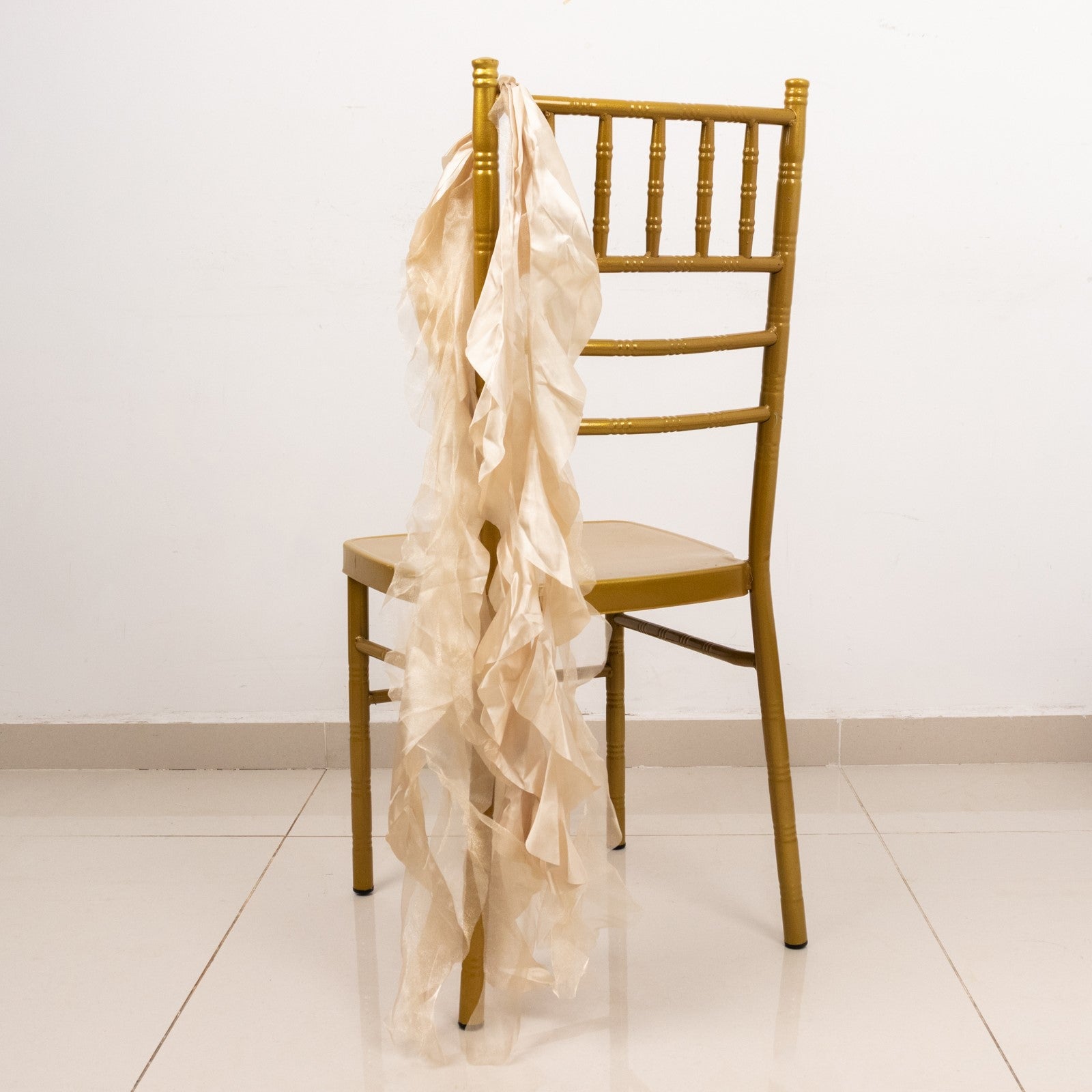 Beige curly chiffon satin chair sash draped on a gold chair.