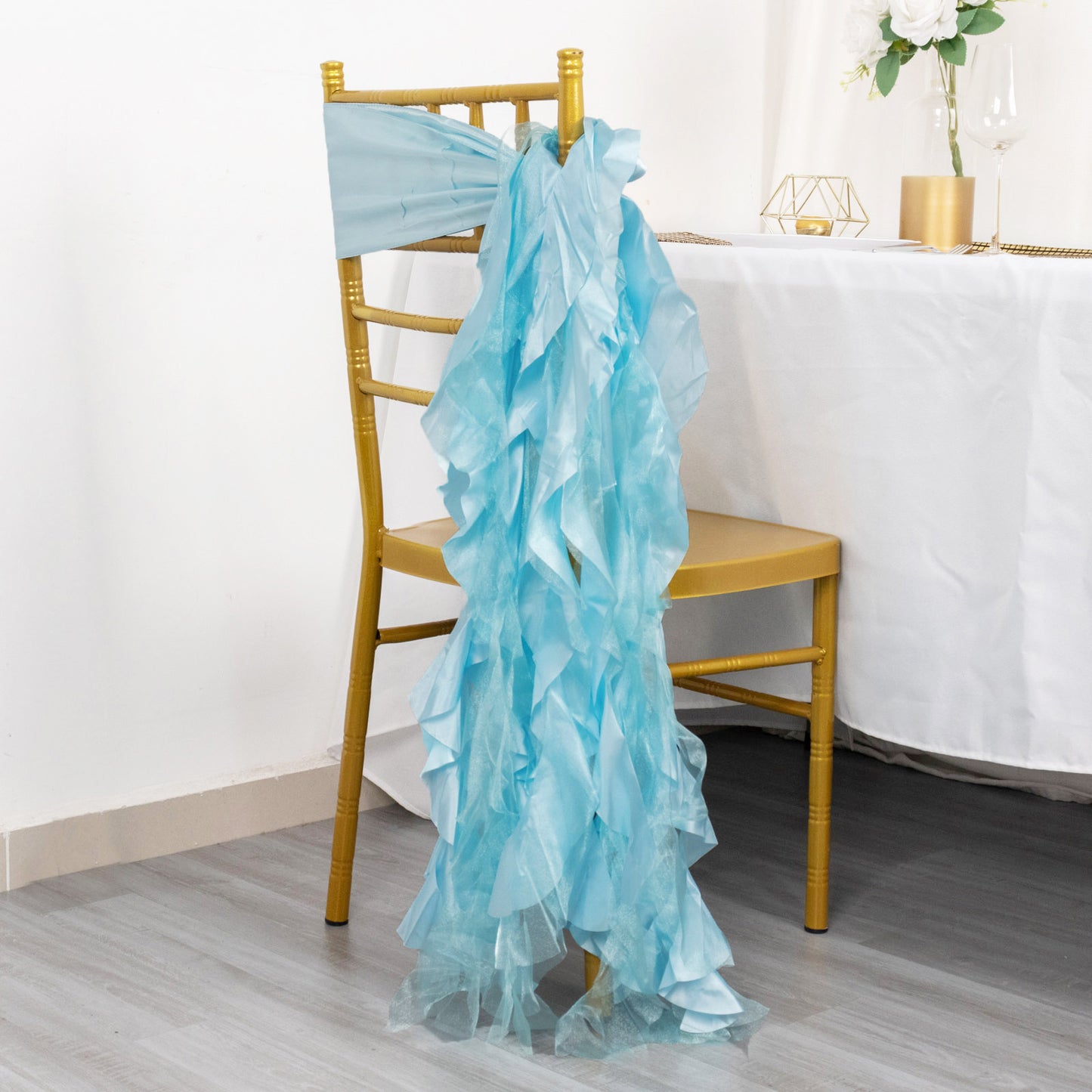 Light blue curly chiffon satin chair sash draped over a gold chair.