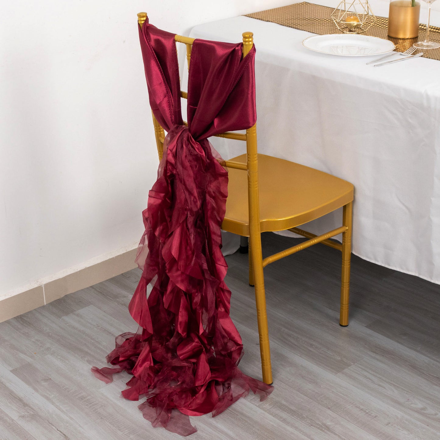 Burgundy chiffon satin chair sash draped on a gold chair.