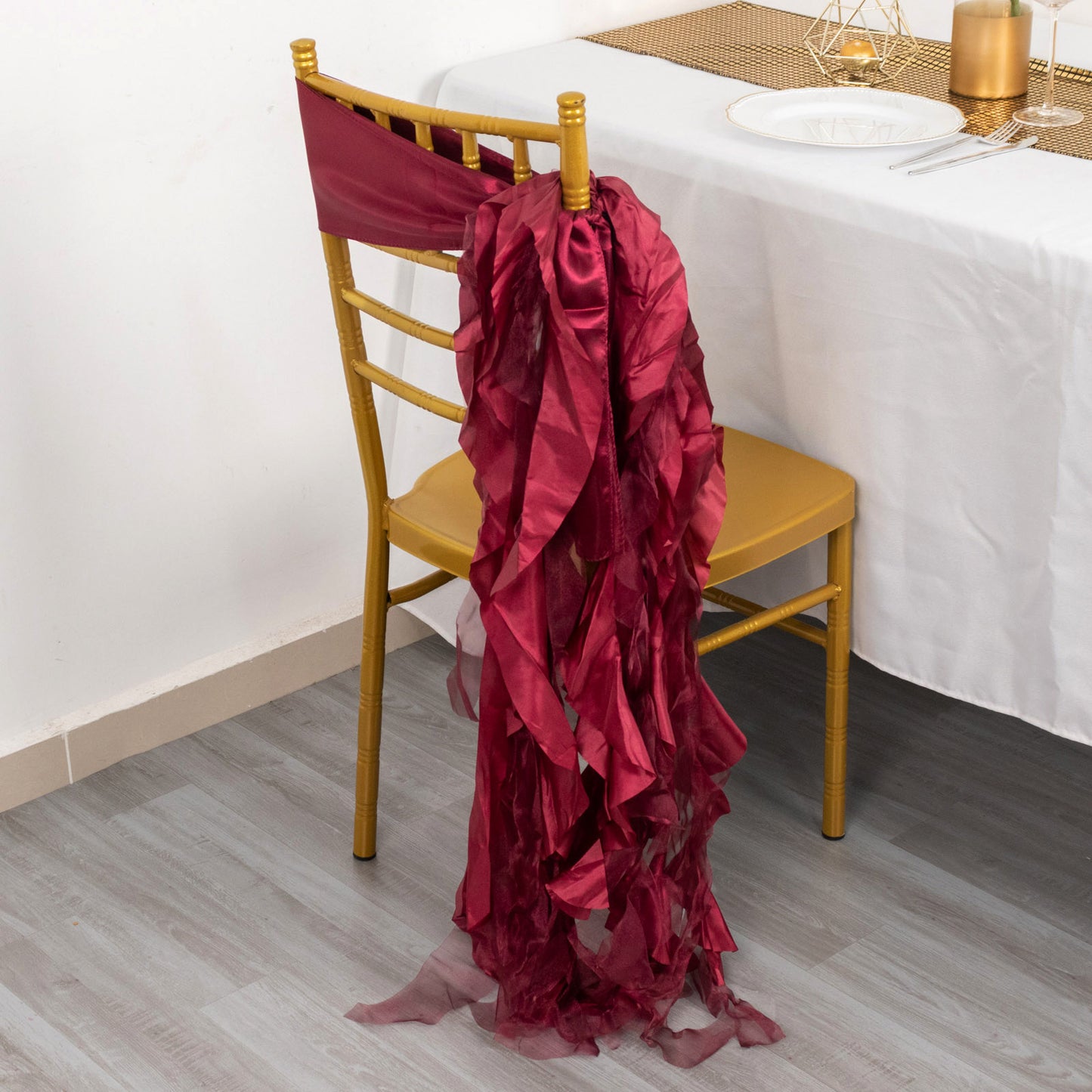 Burgundy chiffon satin chair sash draped on a gold chair.