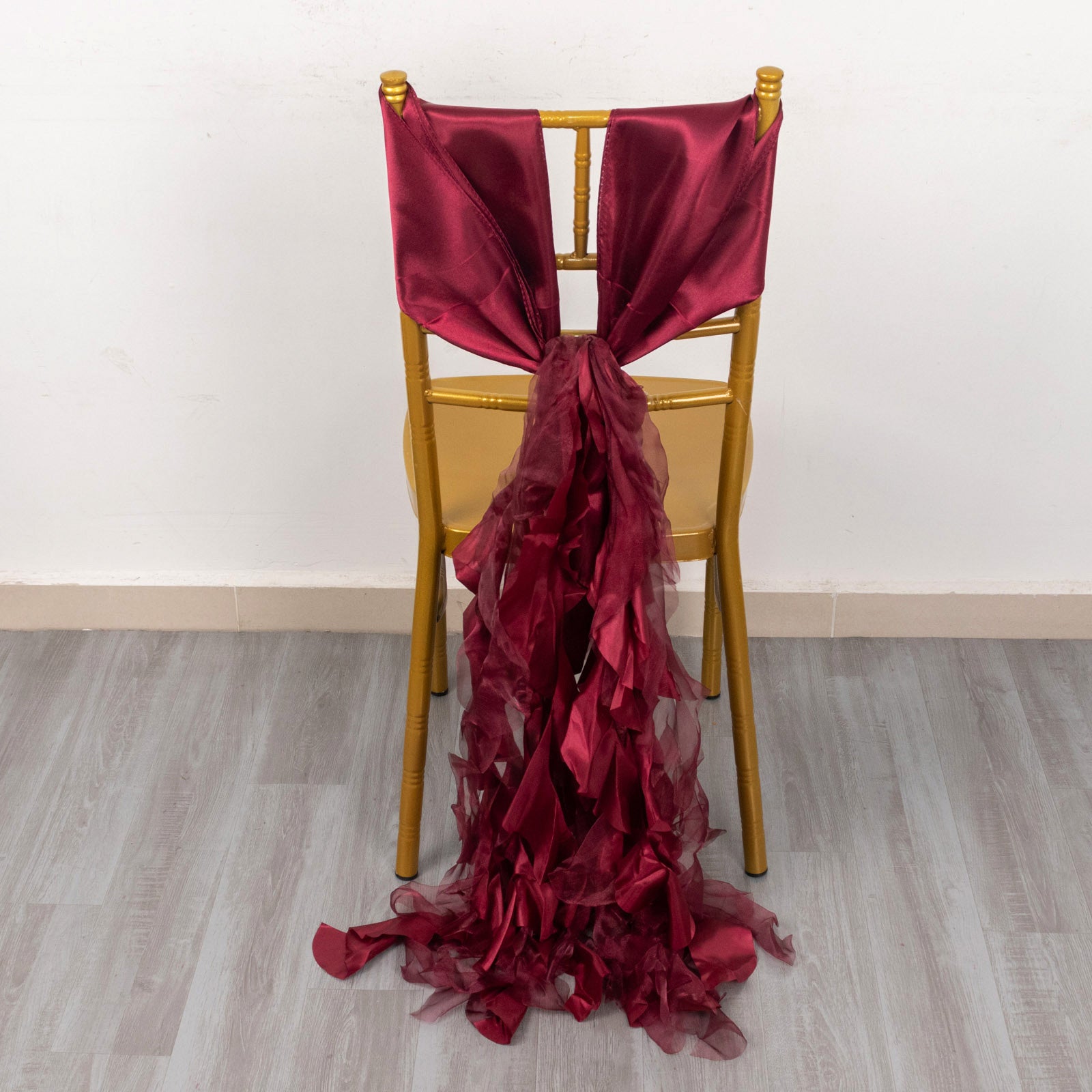 Burgundy chiffon satin chair sash elegantly draped on a gold chair.