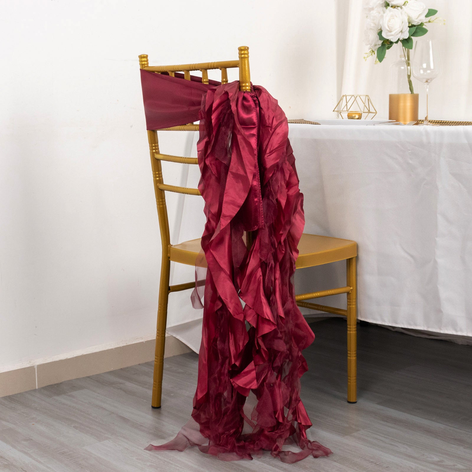 Burgundy chiffon satin chair sash draped on a gold chair.