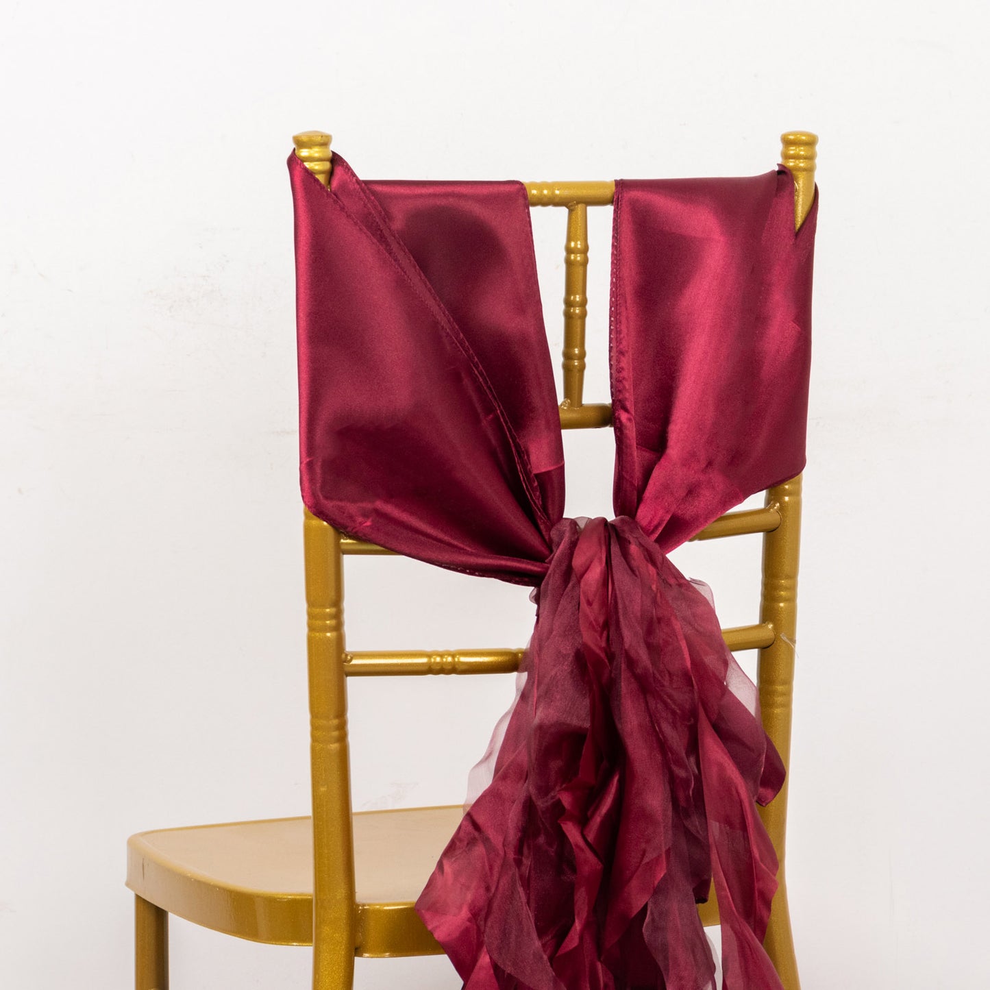 Burgundy chiffon satin chair sash tied on a gold chair.