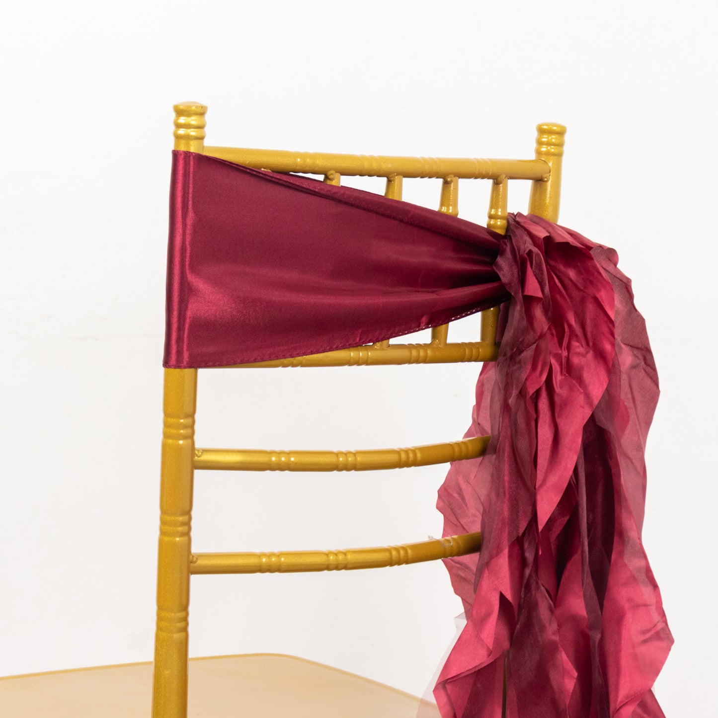 Burgundy chiffon satin chair sash tied around a gold chiavari chair.